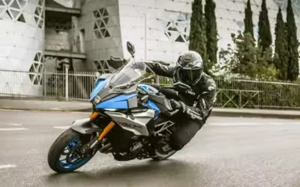 Piloto conduciendo una motocicleta Suzuki deportiva azul en una curva urbana